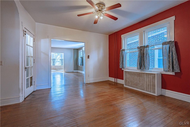 empty room featuring baseboards, radiator, ceiling fan, and hardwood / wood-style flooring