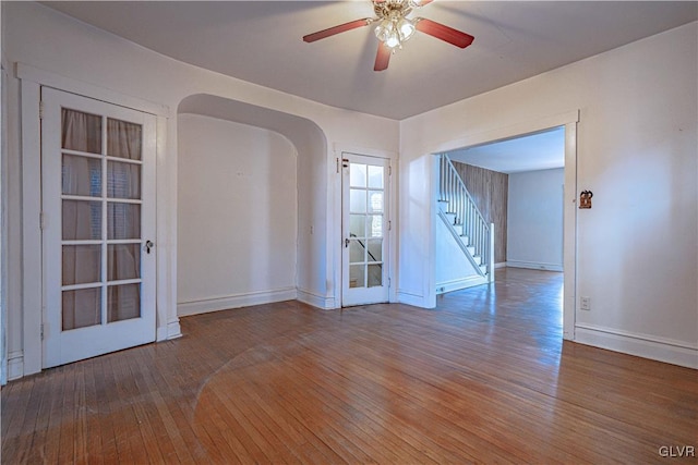 unfurnished room featuring hardwood / wood-style floors, stairway, baseboards, and arched walkways