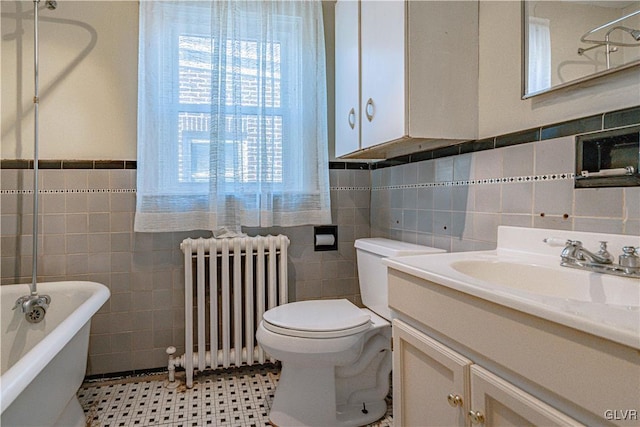 full bath featuring toilet, radiator, tile walls, a freestanding bath, and vanity