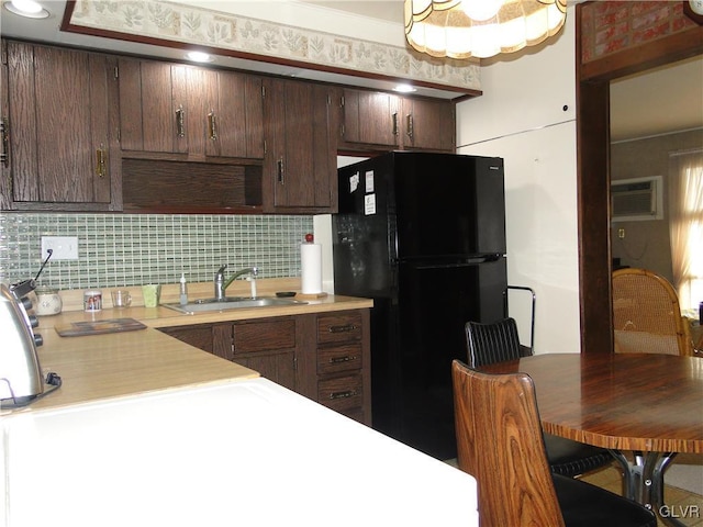 kitchen with light countertops, a wall unit AC, decorative backsplash, freestanding refrigerator, and a sink