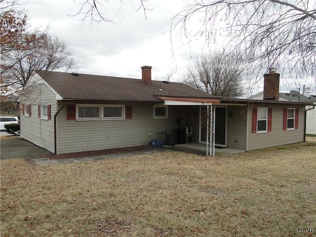 rear view of house with a patio area, a lawn, a chimney, and roof with shingles