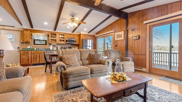 living area with light wood-style flooring, a ceiling fan, a baseboard heating unit, wooden walls, and vaulted ceiling with beams