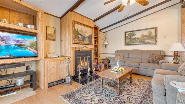 living room with a ceiling fan, wood finished floors, vaulted ceiling with beams, a fireplace with flush hearth, and wood walls