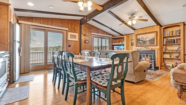 dining area featuring vaulted ceiling with beams, a fireplace with flush hearth, wood walls, built in features, and light wood-style flooring