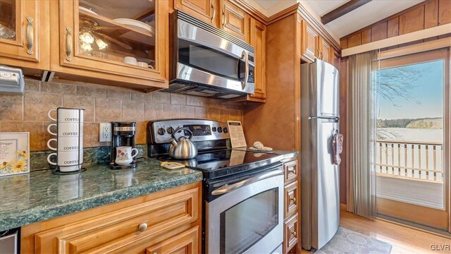 kitchen featuring glass insert cabinets, backsplash, appliances with stainless steel finishes, and brown cabinetry