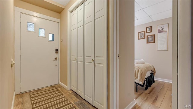 foyer with a drop ceiling, baseboards, and light wood finished floors