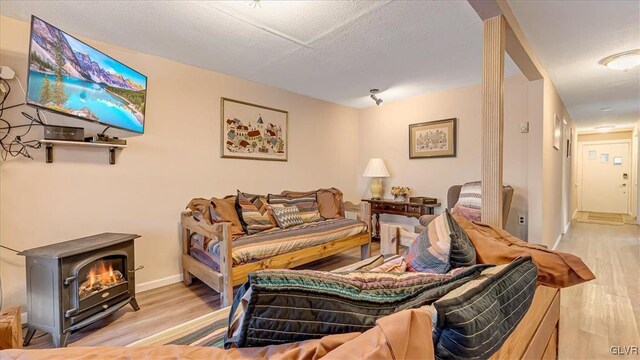 living area with baseboards, a textured ceiling, wood finished floors, and a wood stove