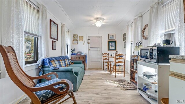 living area featuring light wood finished floors, crown molding, and a ceiling fan