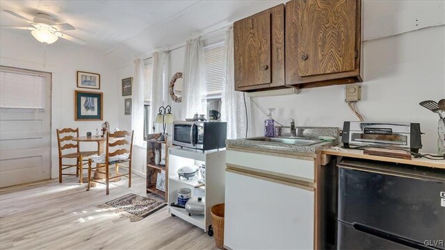 kitchen featuring light wood-style flooring, a sink, stainless steel microwave, fridge, and light countertops