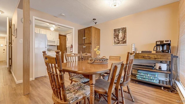 dining room with light wood-style flooring, baseboards, and a textured ceiling