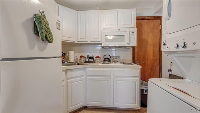 kitchen with tasteful backsplash, light countertops, stacked washing maching and dryer, white appliances, and white cabinetry