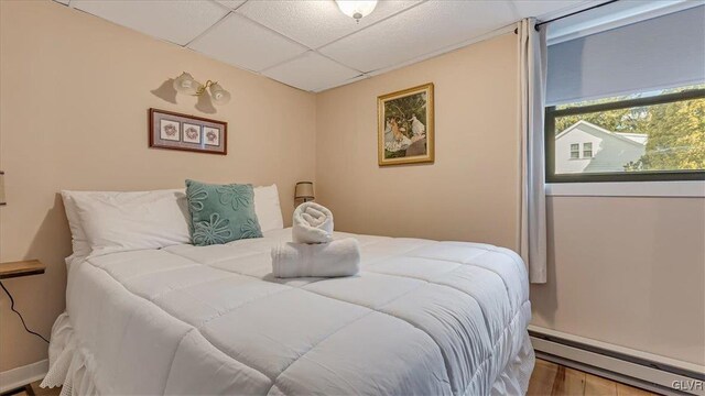 bedroom with a drop ceiling, wood finished floors, and baseboard heating