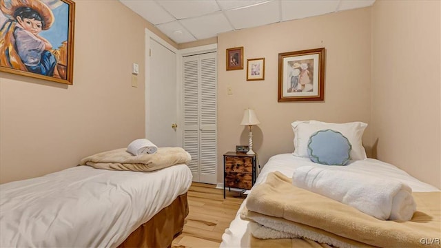 bedroom with light wood-style flooring, a closet, and a drop ceiling