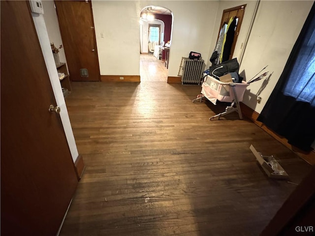 hallway featuring wood finished floors, arched walkways, and baseboards