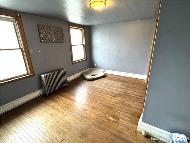 unfurnished room featuring baseboards, wood-type flooring, and radiator