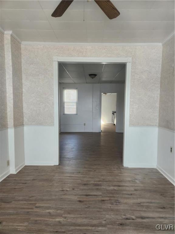 empty room with a ceiling fan, wood finished floors, wainscoting, and crown molding