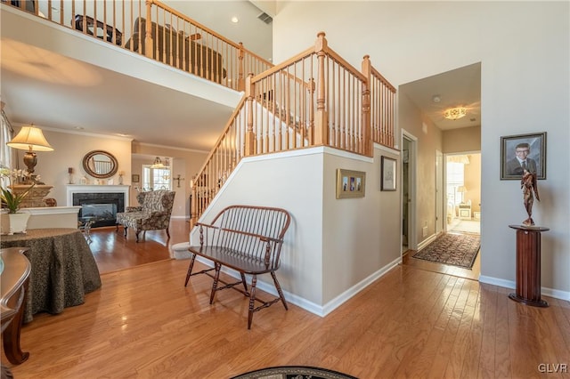 stairway featuring baseboards, hardwood / wood-style flooring, a towering ceiling, a glass covered fireplace, and crown molding