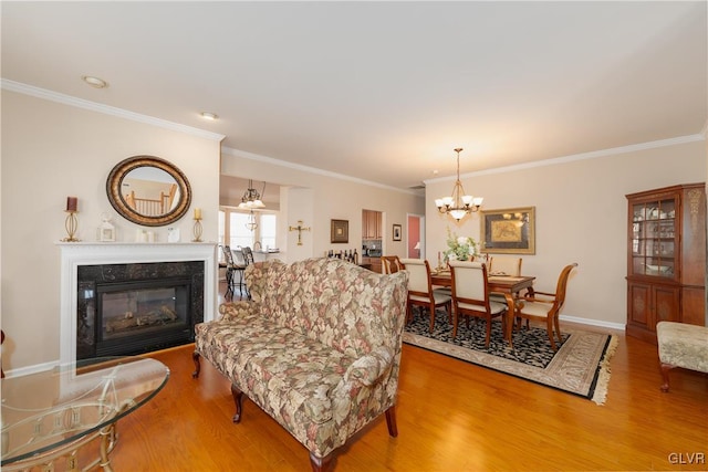living room featuring a notable chandelier, a glass covered fireplace, crown molding, baseboards, and wood finished floors
