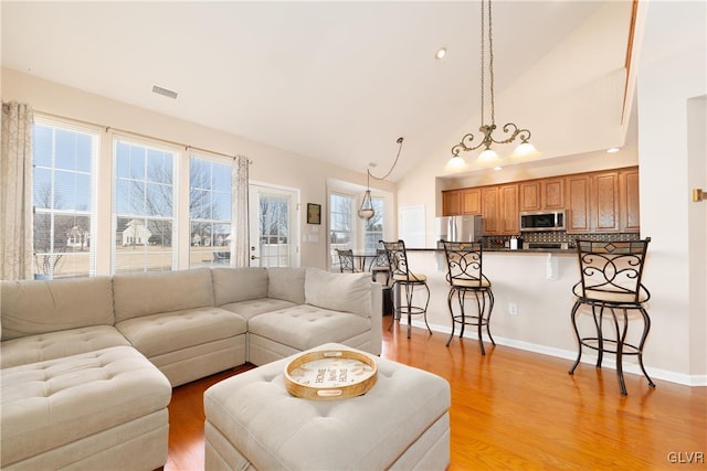 living room with baseboards, visible vents, light wood finished floors, and high vaulted ceiling
