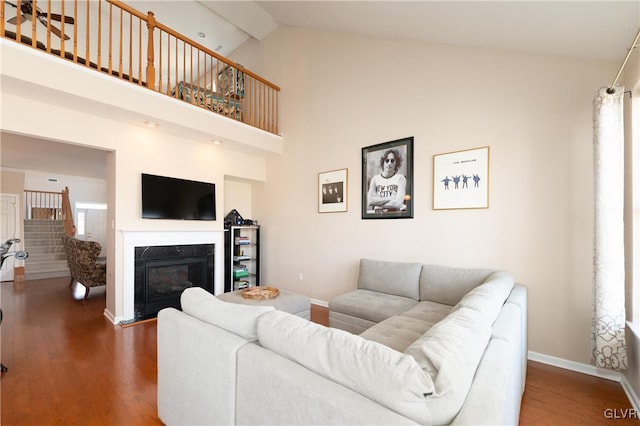 living area featuring wood finished floors, high vaulted ceiling, a premium fireplace, and baseboards