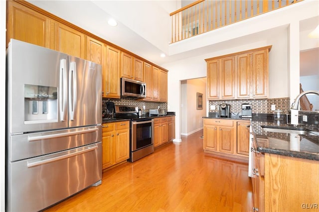 kitchen featuring a sink, stainless steel appliances, dark stone countertops, tasteful backsplash, and light wood-type flooring