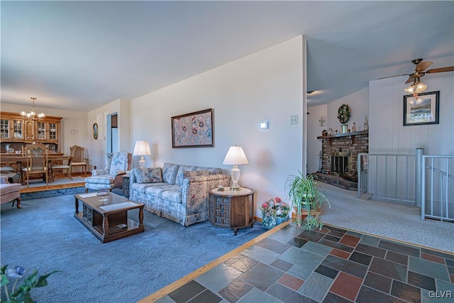 living room featuring dark colored carpet, stone finish flooring, a brick fireplace, and ceiling fan with notable chandelier