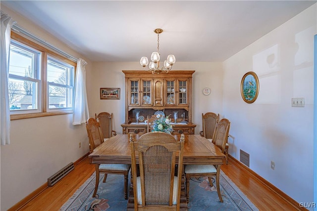 dining area with light wood-style flooring, a notable chandelier, baseboards, and visible vents