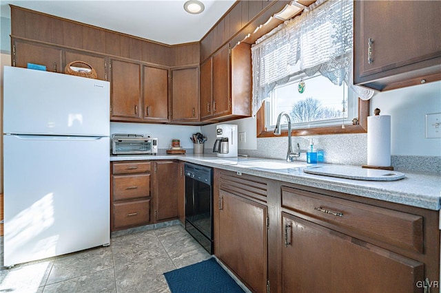 kitchen featuring dishwasher, light countertops, freestanding refrigerator, and a sink