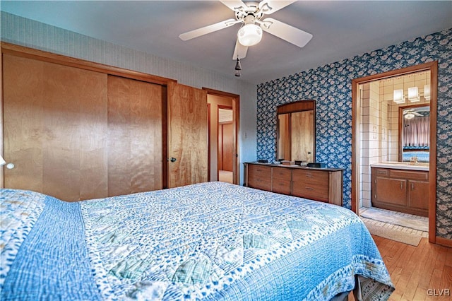 bedroom featuring light wood finished floors, wallpapered walls, ceiling fan, a closet, and a sink