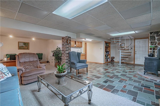 living area with a drop ceiling, stairway, a wood stove, and baseboards