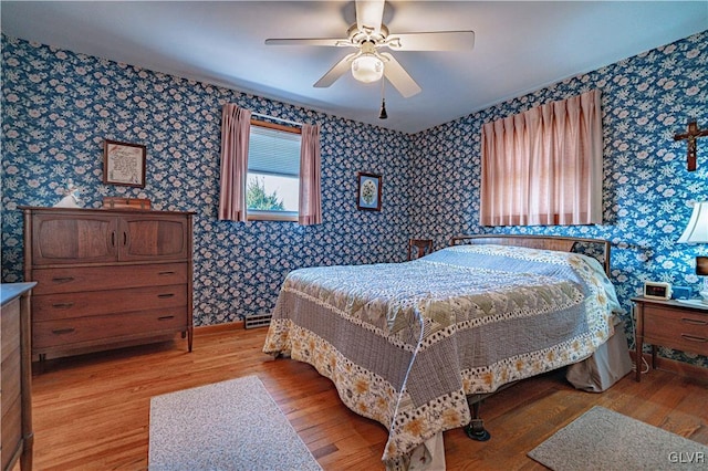 bedroom with light wood finished floors, baseboards, wallpapered walls, and ceiling fan