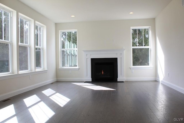 unfurnished living room featuring plenty of natural light, visible vents, a fireplace with flush hearth, and wood finished floors