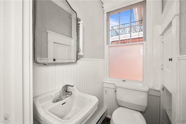 half bathroom featuring a sink, toilet, and wainscoting