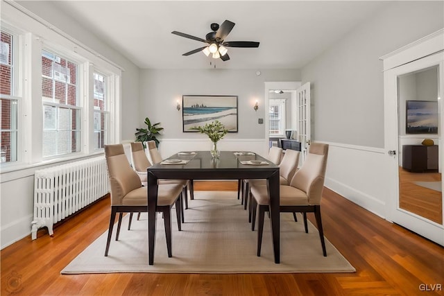 dining space with radiator, wood finished floors, wainscoting, and ceiling fan