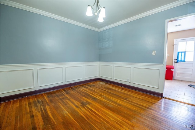 spare room with a notable chandelier, wainscoting, crown molding, and dark wood-type flooring