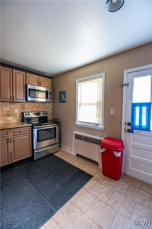 kitchen featuring backsplash, radiator heating unit, appliances with stainless steel finishes, light tile patterned flooring, and light countertops