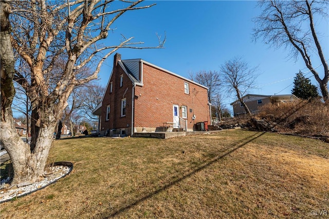 rear view of property with brick siding, a chimney, and a yard