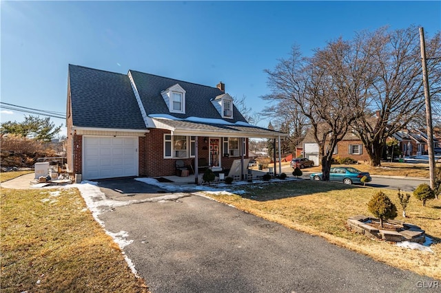 new england style home featuring a front lawn, aphalt driveway, a porch, a garage, and brick siding