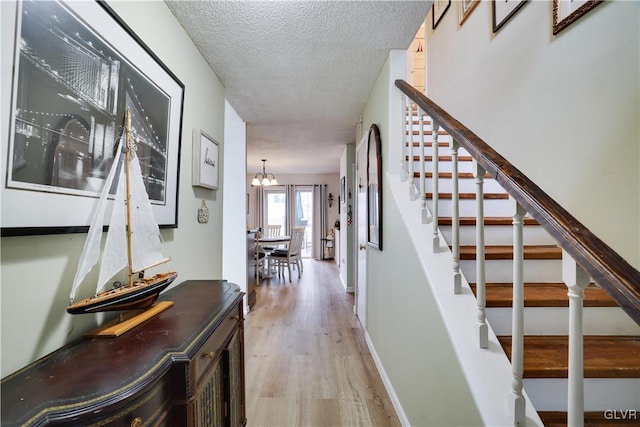 corridor featuring baseboards, stairway, wood finished floors, a notable chandelier, and a textured ceiling