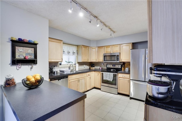 kitchen with a sink, dark countertops, appliances with stainless steel finishes, and light brown cabinetry