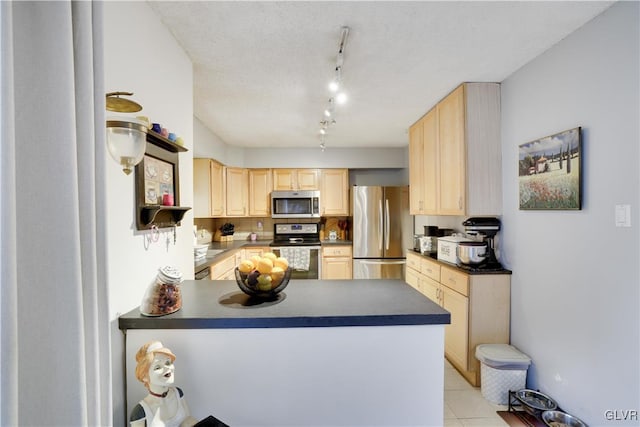 kitchen featuring dark countertops, light brown cabinets, light tile patterned floors, appliances with stainless steel finishes, and a peninsula