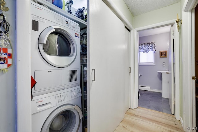 clothes washing area with laundry area, wood finished floors, a textured ceiling, stacked washer / drying machine, and a baseboard radiator