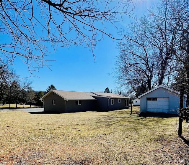 back of property with an outdoor structure, a detached garage, and a yard