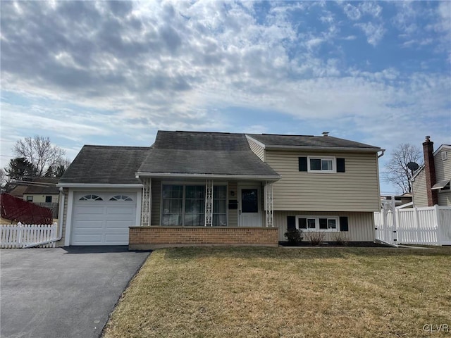 tri-level home featuring a front yard, an attached garage, fence, and aphalt driveway