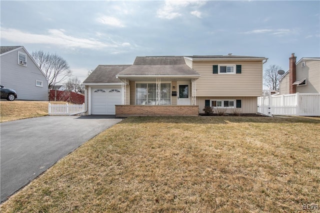 split level home featuring aphalt driveway, a garage, a front yard, and fence