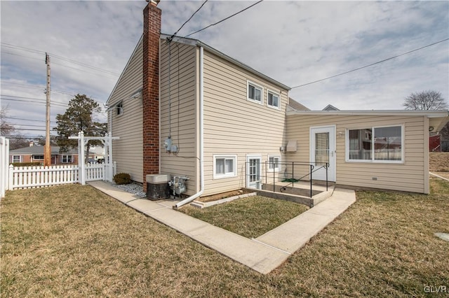 rear view of house with central air condition unit, a lawn, fence, and a chimney