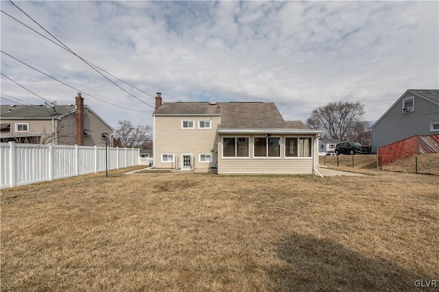 rear view of house featuring a chimney, a yard, and fence