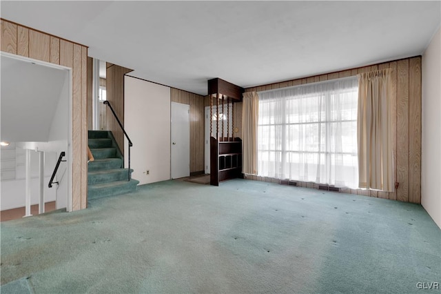 unfurnished living room with wooden walls, visible vents, stairs, and carpet