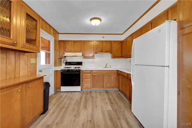 kitchen with under cabinet range hood, gas range, light countertops, brown cabinets, and freestanding refrigerator