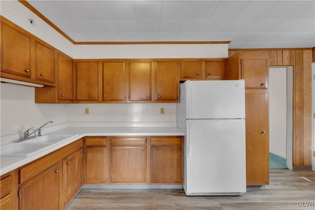 kitchen with brown cabinets, freestanding refrigerator, light wood-style floors, and a sink